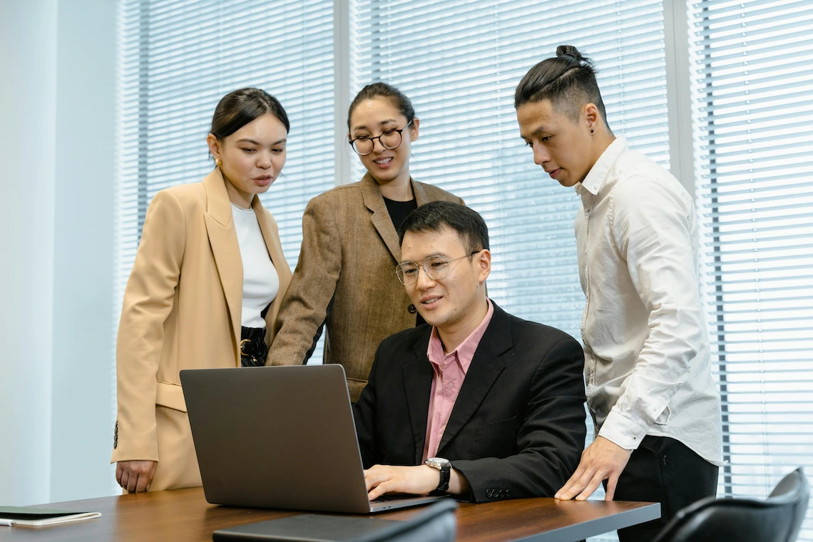 imagem de uma pessoa mexendo em um notebook e outras pessoas ao seu redor