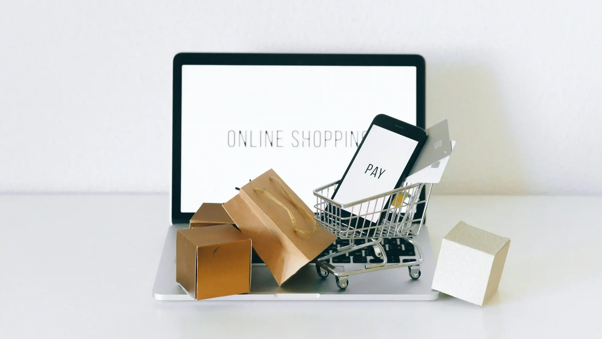 Imagem de um notebook e miniatura de um carrinho de compras e sacolas.
